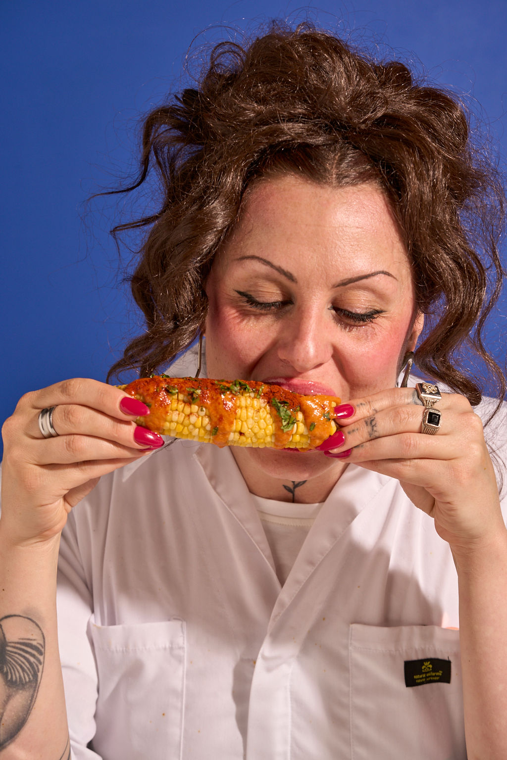 Biting into a Tikka-sauced corn cob against a cobalt wall